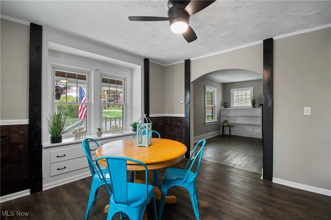 Dining space with dark wood-type flooring, ornamental molding, arched walkways, a textured ceiling, and a ceiling fan