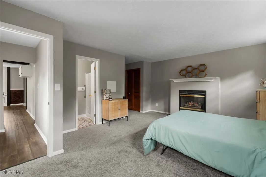 Carpeted bedroom with a glass covered fireplace, a closet, ensuite bath, and a textured ceiling