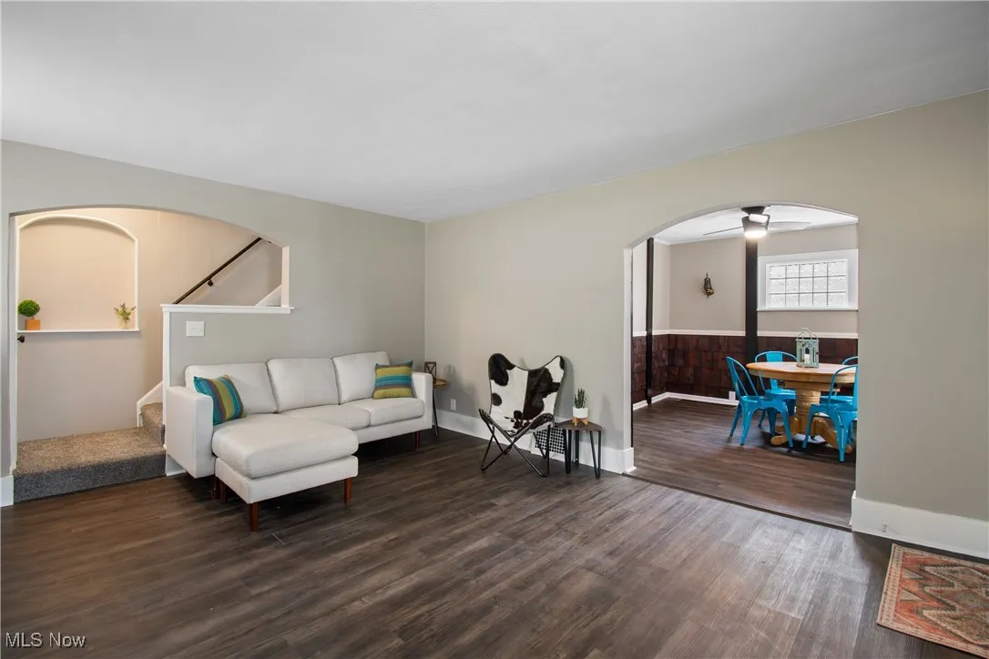 Living area with arched walkways, dark wood-type flooring, stairway, and a ceiling fan