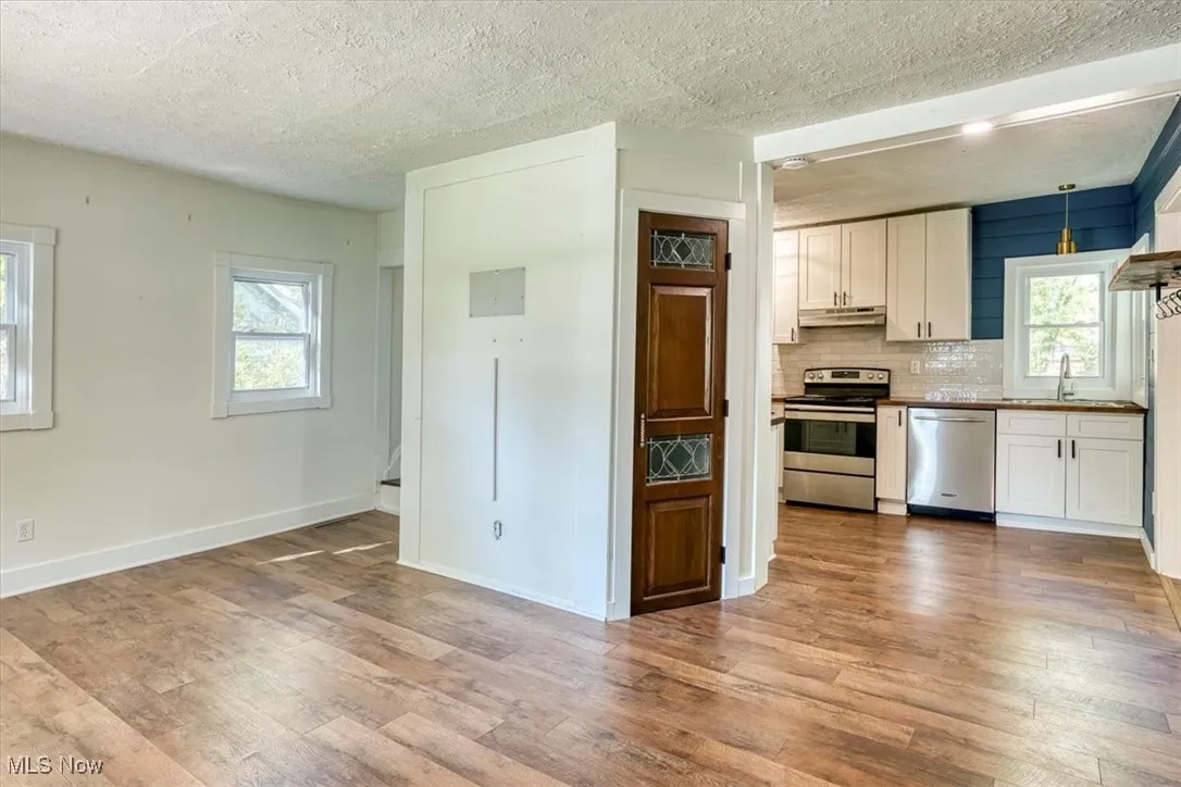Kitchen featuring appliances with stainless steel finishes, tasteful backsplash, white cabinets, light wood-style flooring, and a textured ceiling