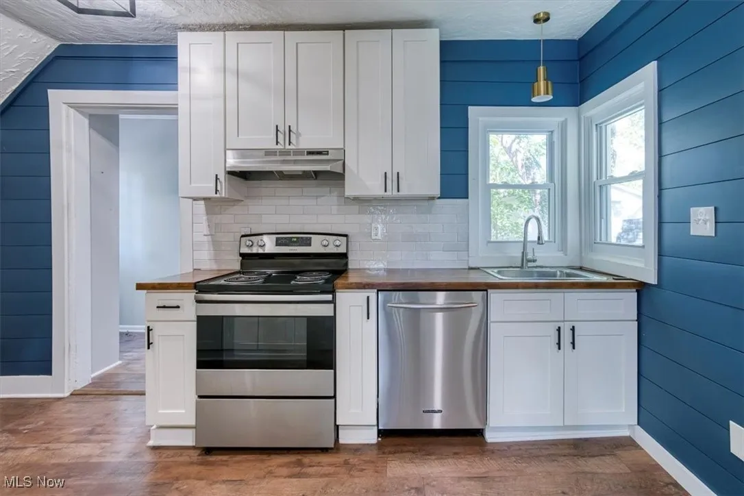 Kitchen featuring appliances with stainless steel finishes, white cabinets, wooden walls, and a textured ceiling