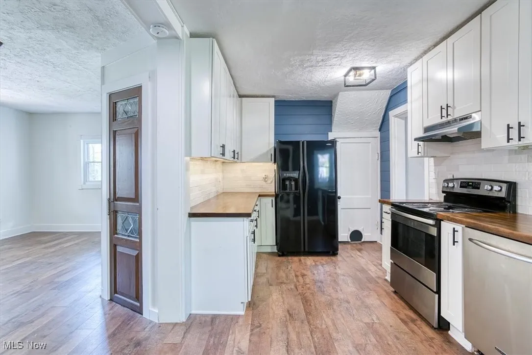 Kitchen featuring stainless steel appliances, backsplash, white cabinets, a textured ceiling, and wooden counters