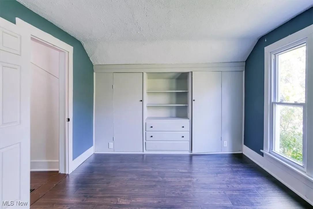 Unfurnished bedroom featuring a textured ceiling, vaulted ceiling, dark wood-type flooring, and a closet