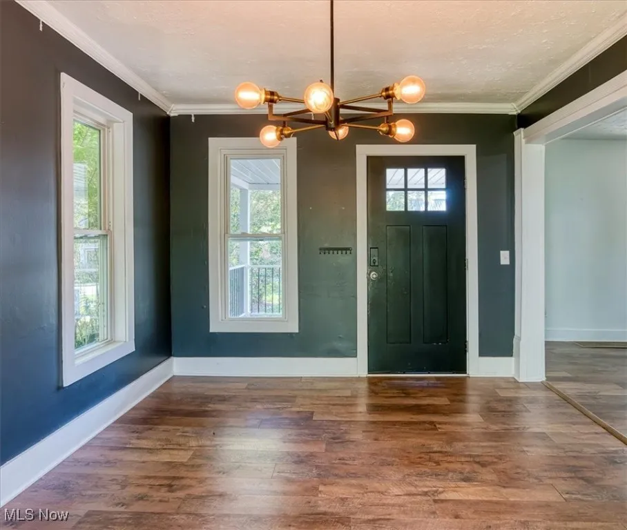 Foyer with wood-type flooring, healthy amount of natural light, a textured ceiling, crown molding, and a chandelier