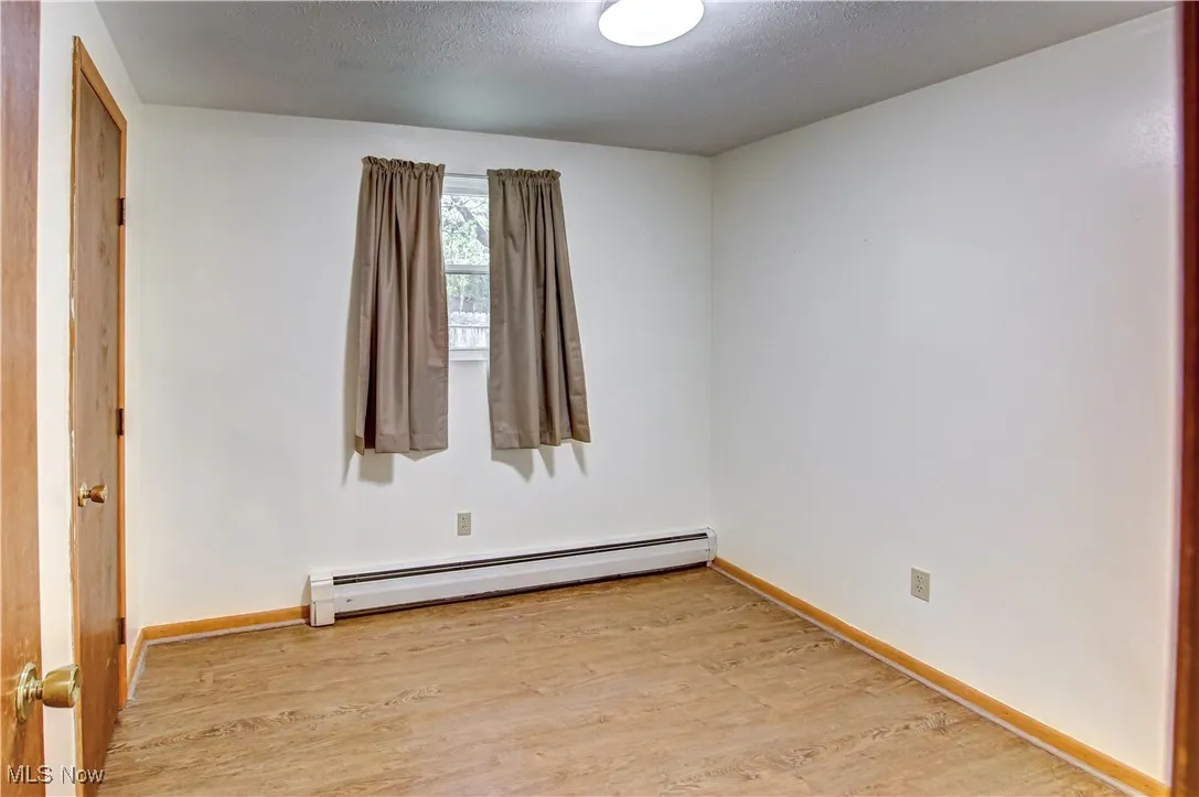 Bedroom with light wood-style laminate flooring, a baseboard radiator, and a textured ceiling