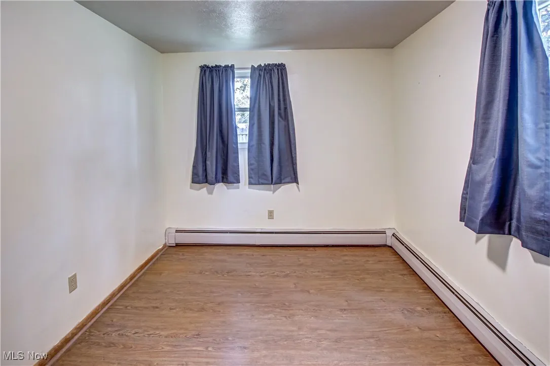 Master bedroom featuring baseboard heating, light wood-type laminate flooring, and a textured ceiling