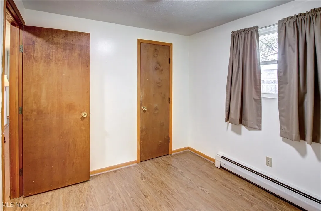 Unfurnished bedroom featuring a baseboard heating unit, light wood-style laminate flooring, and a textured ceiling