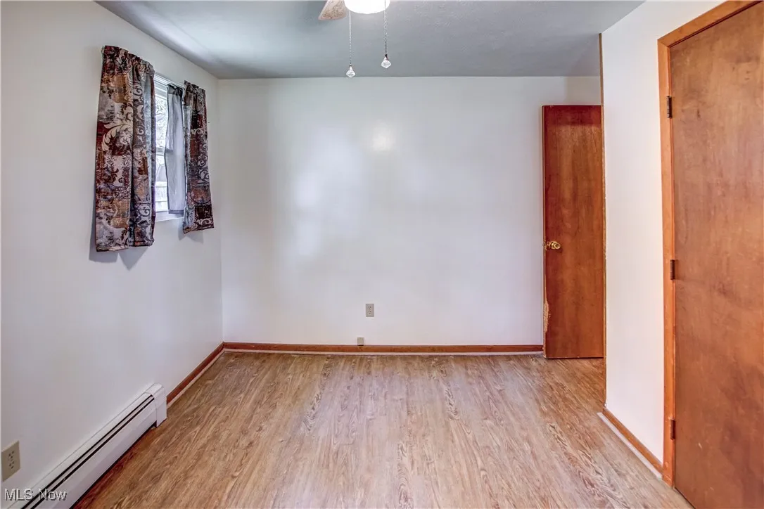 Bedroom with a baseboard radiator, light wood finished laminate floors, and ceiling fan