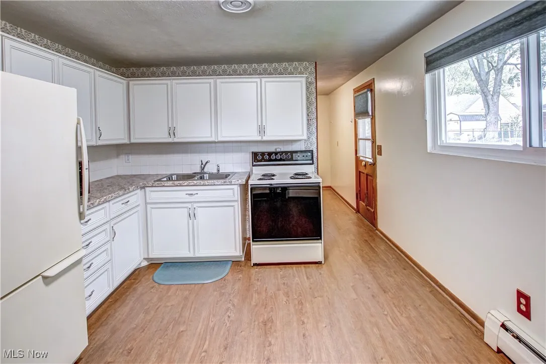 Kitchen with white appliances, light countertops, light wood-type laminate flooring, white cabinets, and baseboard heating