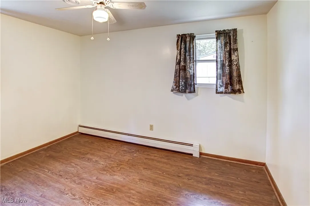Bedroom featuring baseboard heating, wood finished laminate floors, and a ceiling fan