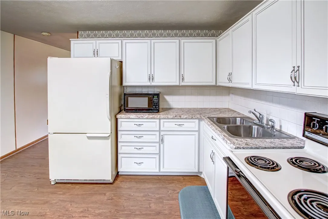 Kitchen featuring white cabinetry, white appliances, backsplash, and light wood-type laminate flooring