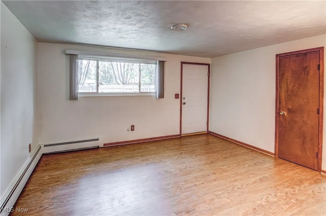 Unfurnished Living room with a baseboard heat, light wood-type laminate floors, and a textured ceiling
