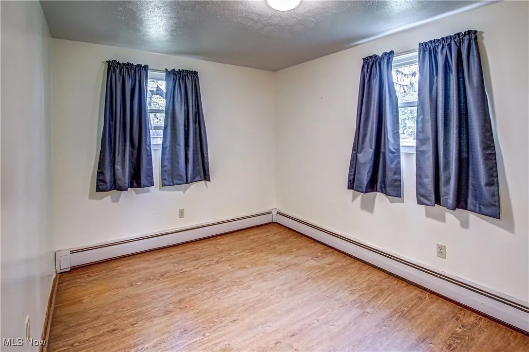 Master bedroom featuring wood finished laminate floors, a baseboard heating unit, and a textured ceiling