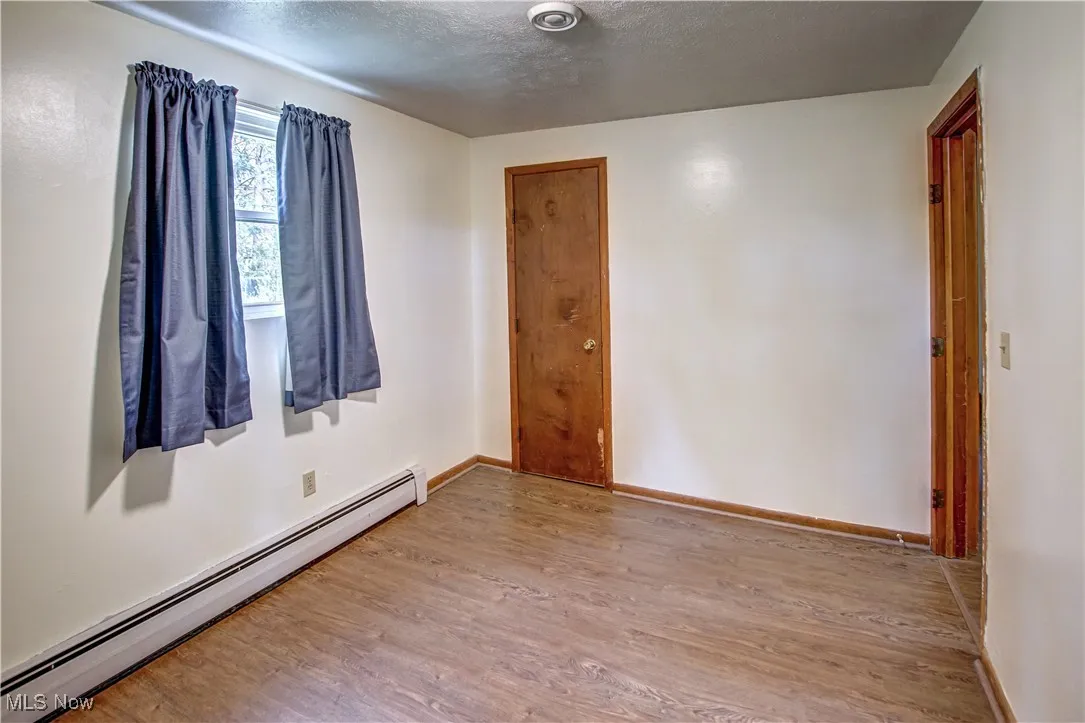 Master bedroom featuring a baseboard radiator, light wood-style laminate flooring, and a textured ceiling