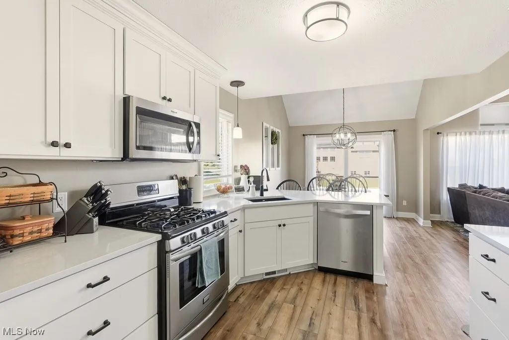 Kitchen featuring appliances with stainless steel finishes, white cabinetry, open floor plan, a peninsula, and vaulted ceiling
