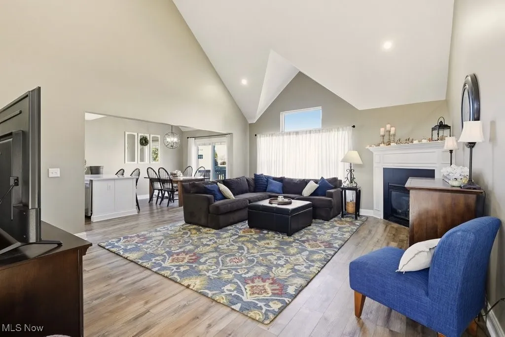 Living area with high vaulted ceiling, light wood finished floors, recessed lighting, a glass covered fireplace, and a chandelier