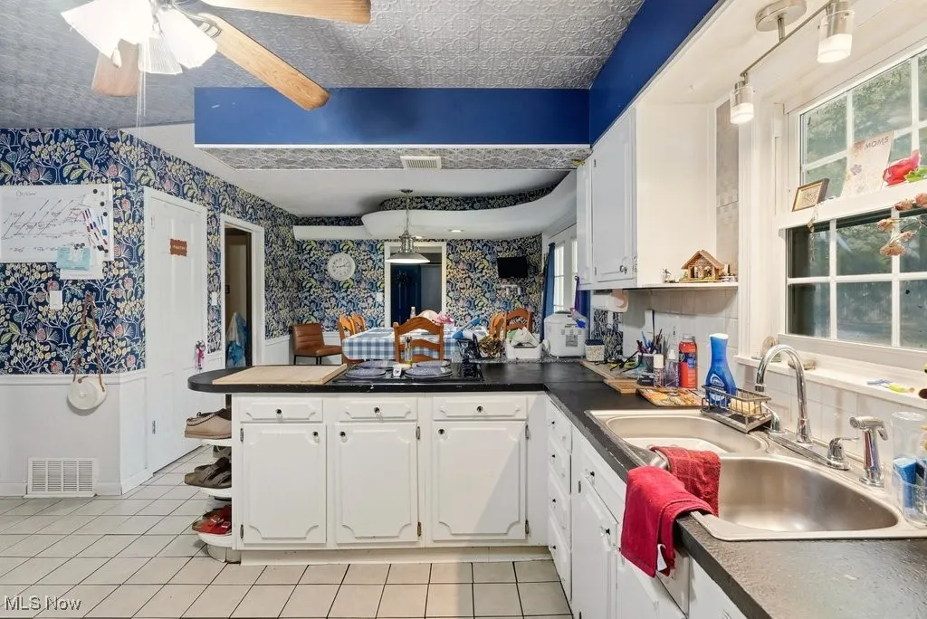 Kitchen featuring a peninsula, a ceiling fan, white cabinetry, wallpapered walls, and wainscoting