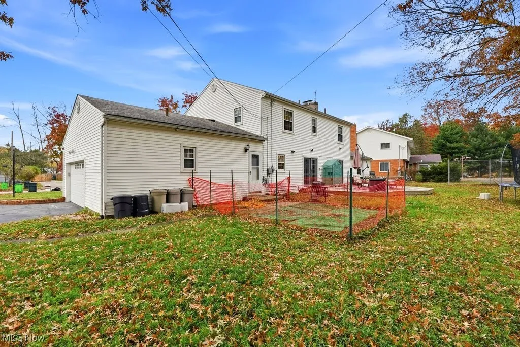 Rear view of property featuring a patio area, a lawn, a garage, asphalt driveway, and a trampoline