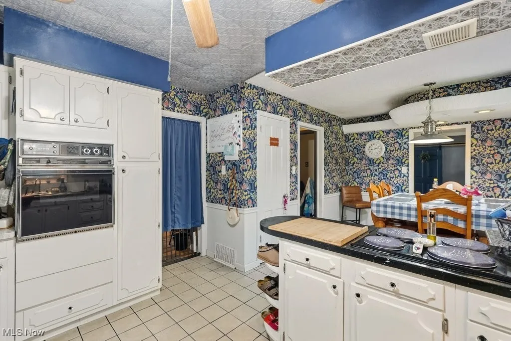 Kitchen with white cabinetry, black appliances, dark countertops, wallpapered walls, and ceiling fan