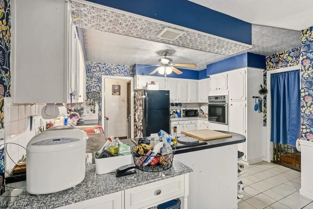 Kitchen featuring white cabinets, wallpapered walls, light tile patterned flooring, black appliances, and ceiling fan