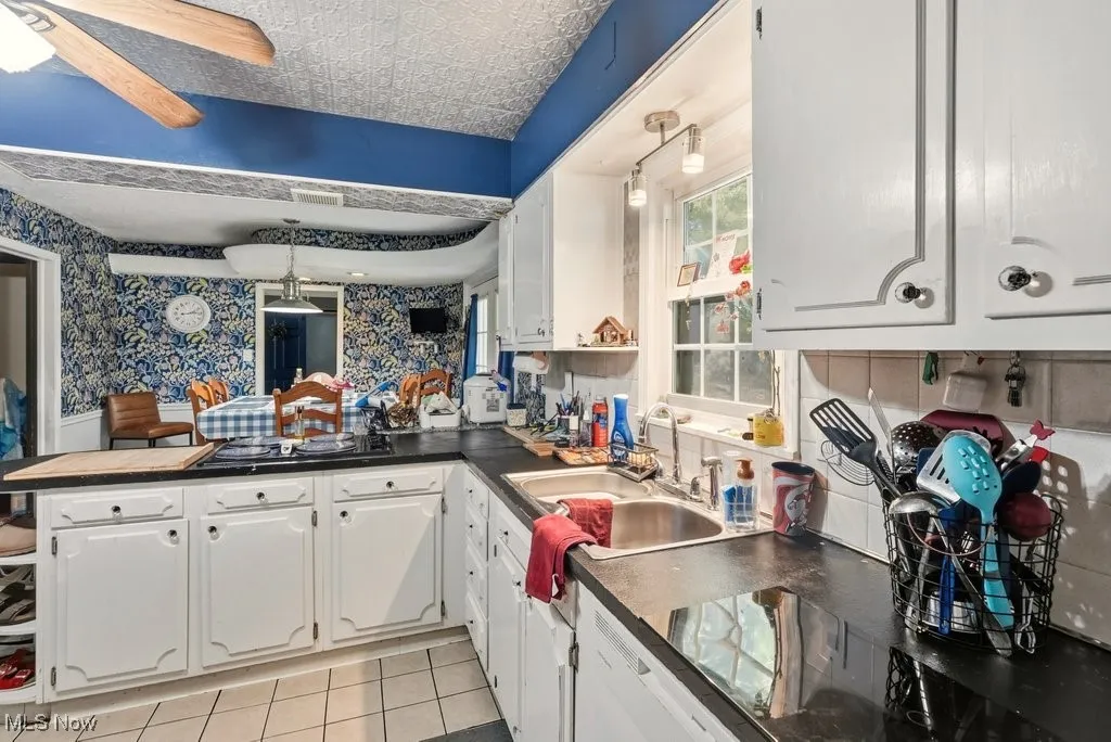 Kitchen with a peninsula, dark countertops, white cabinetry, an ornate ceiling, and wallpapered walls