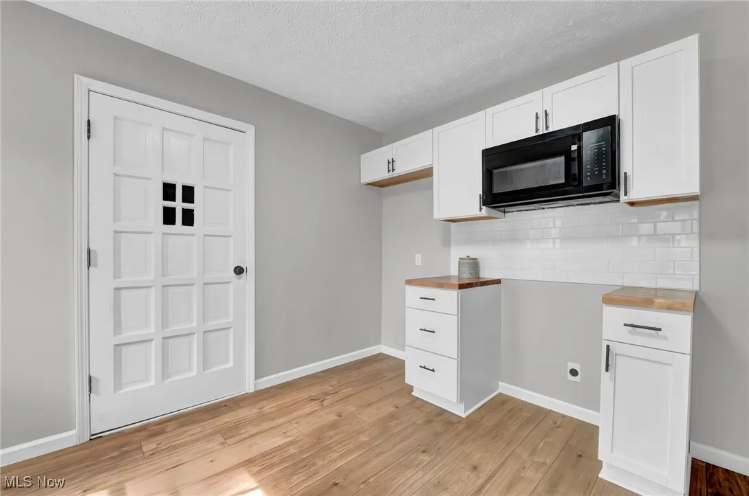 Kitchen featuring white cabinets, black microwave, a textured ceiling, light wood finished floors, and backsplash