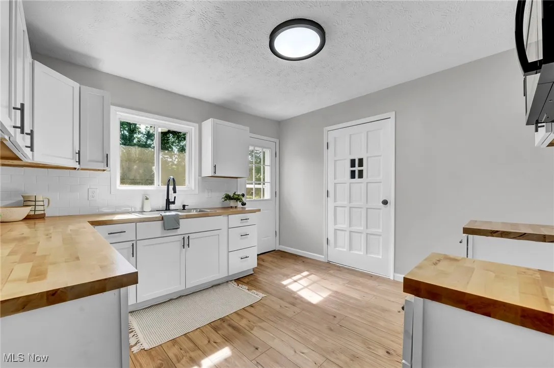 Kitchen with wooden counters, white cabinets, decorative backsplash, and a textured ceiling