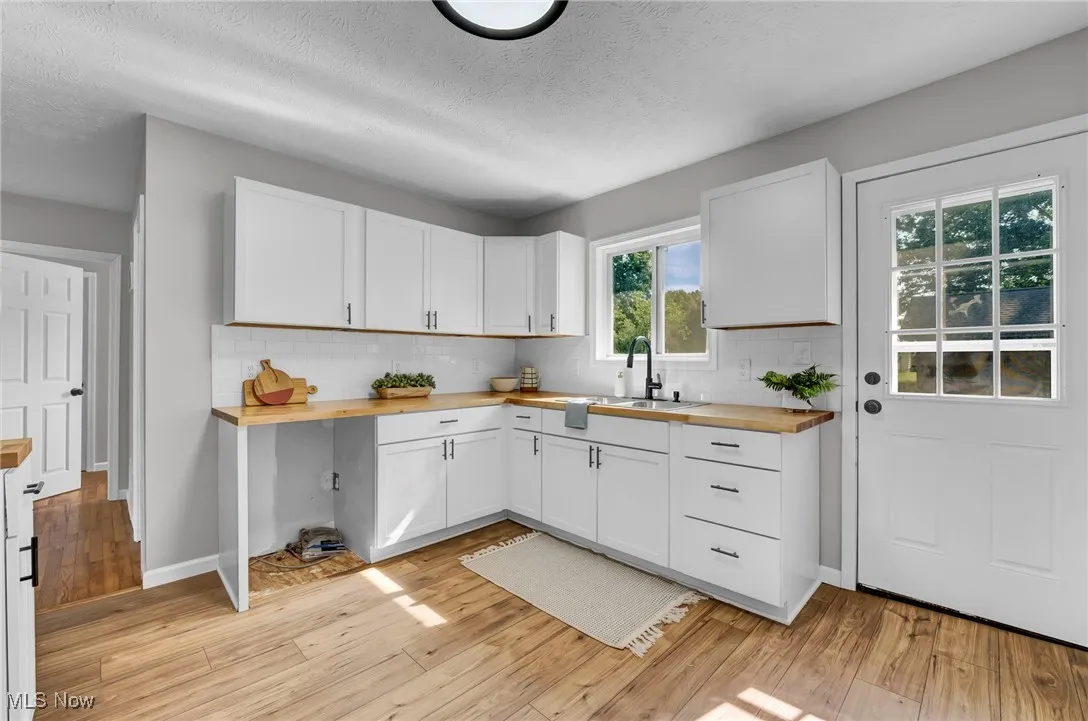 Kitchen with wooden counters, white cabinetry, a textured ceiling, light wood-style flooring, and tasteful backsplash