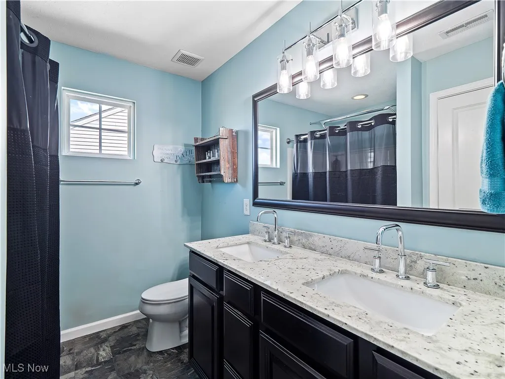 Full bathroom featuring double vanity, a shower with curtain, and dark stone finish floors