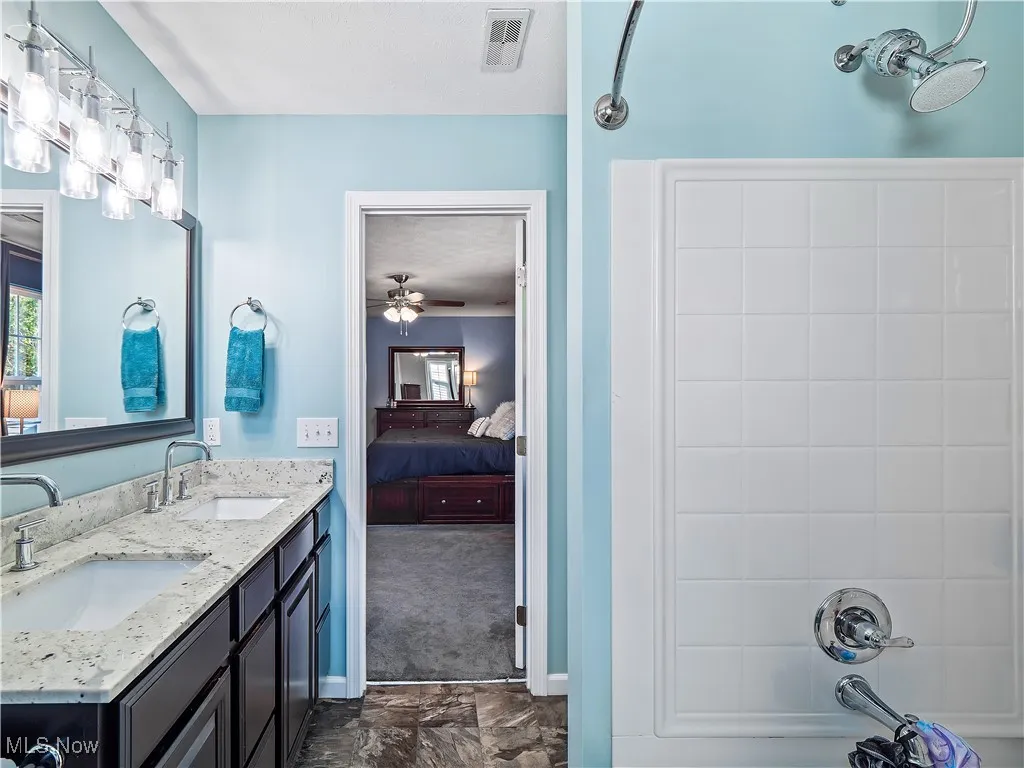 Full bath with ensuite bathroom, double vanity, washtub / shower combination, ceiling fan, and dark carpet
