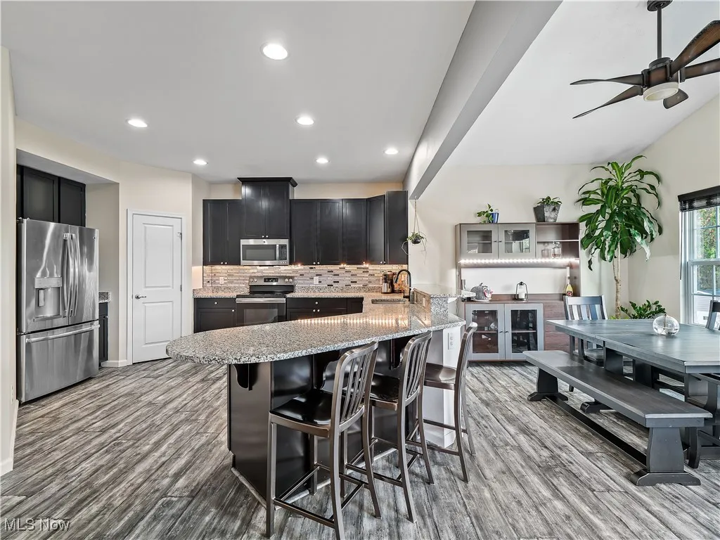 Kitchen with a peninsula, a kitchen bar, appliances with stainless steel finishes, light stone counters, and backsplash