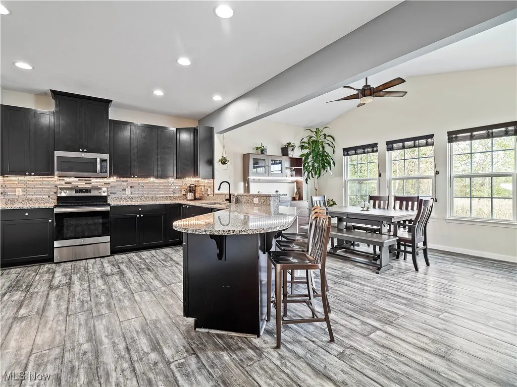 Kitchen with dark cabinets, appliances with stainless steel finishes, a breakfast bar, light stone counters, and a peninsula