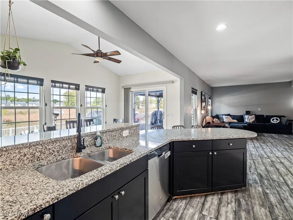 Kitchen featuring light stone counters, open floor plan, dark cabinetry, stainless steel dishwasher, and dark wood-style floors