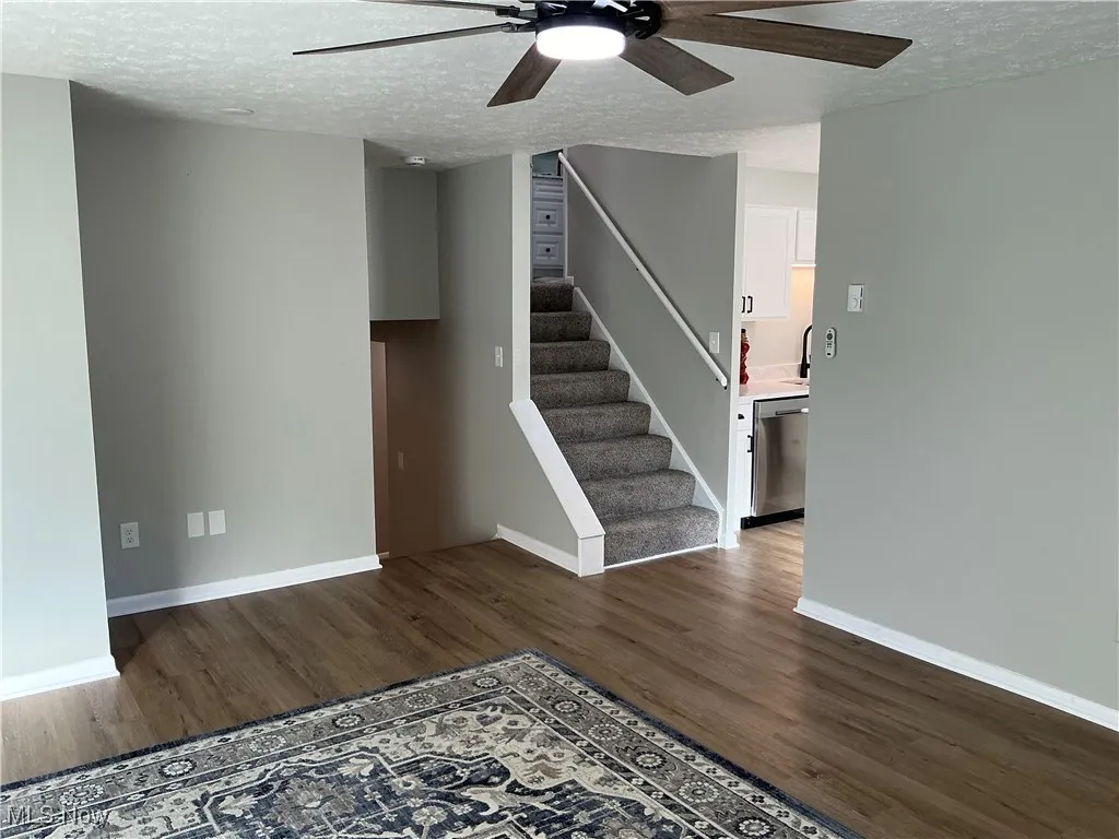 Living room featuring ceiling fan, a textured ceiling, stairway, and dark wood-style floors