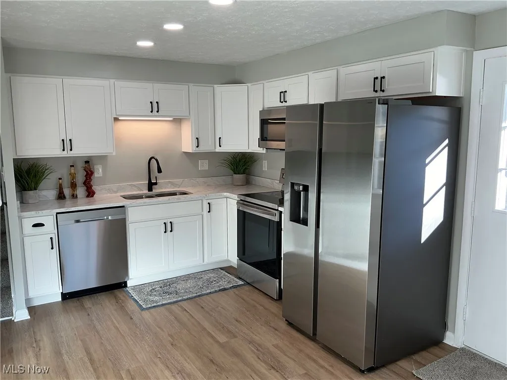 Kitchen featuring appliances with stainless steel finishes, a textured ceiling, white cabinets, light wood-style flooring, and light stone countertops