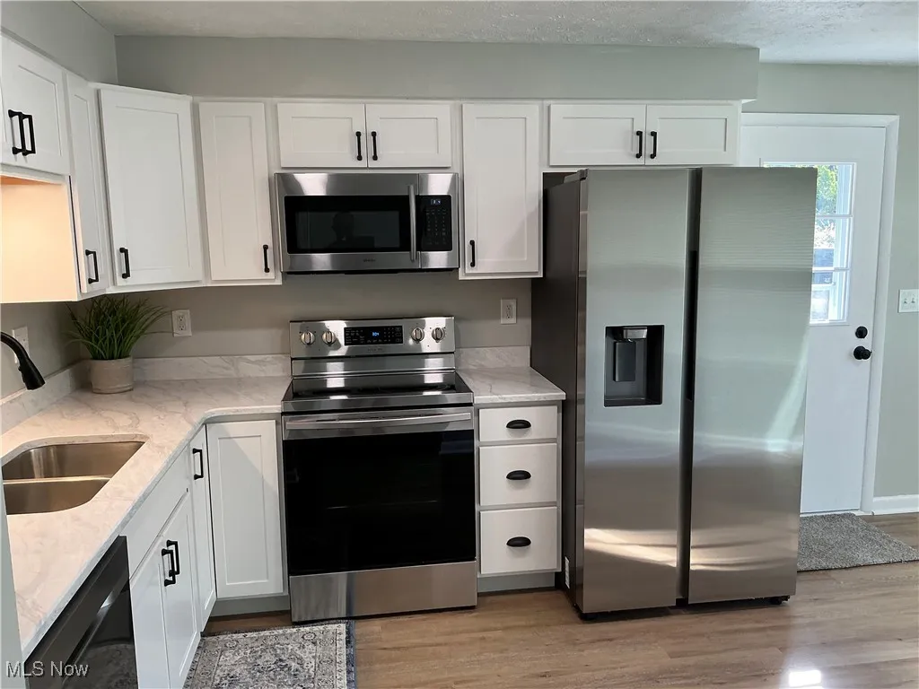 Kitchen with appliances with stainless steel finishes, light stone counters, white cabinets, and a textured ceiling