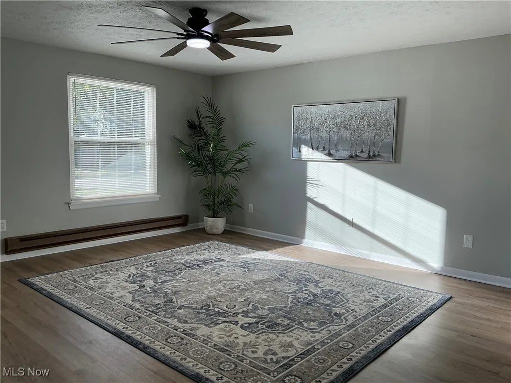 Living room with a textured ceiling, baseboard heating, light wood finished floors, and ceiling fan