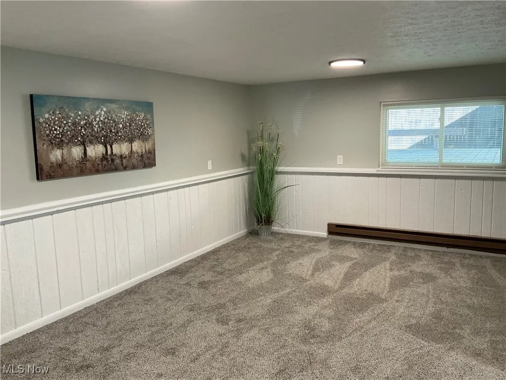 Carpeted room with wainscoting, baseboard heating, a textured ceiling, and wooden walls