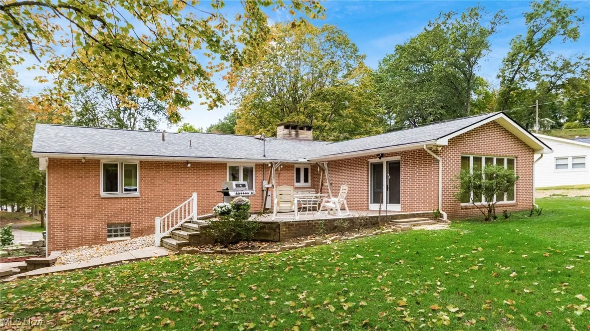 Back of property featuring a yard, brick siding, a chimney, and a deck