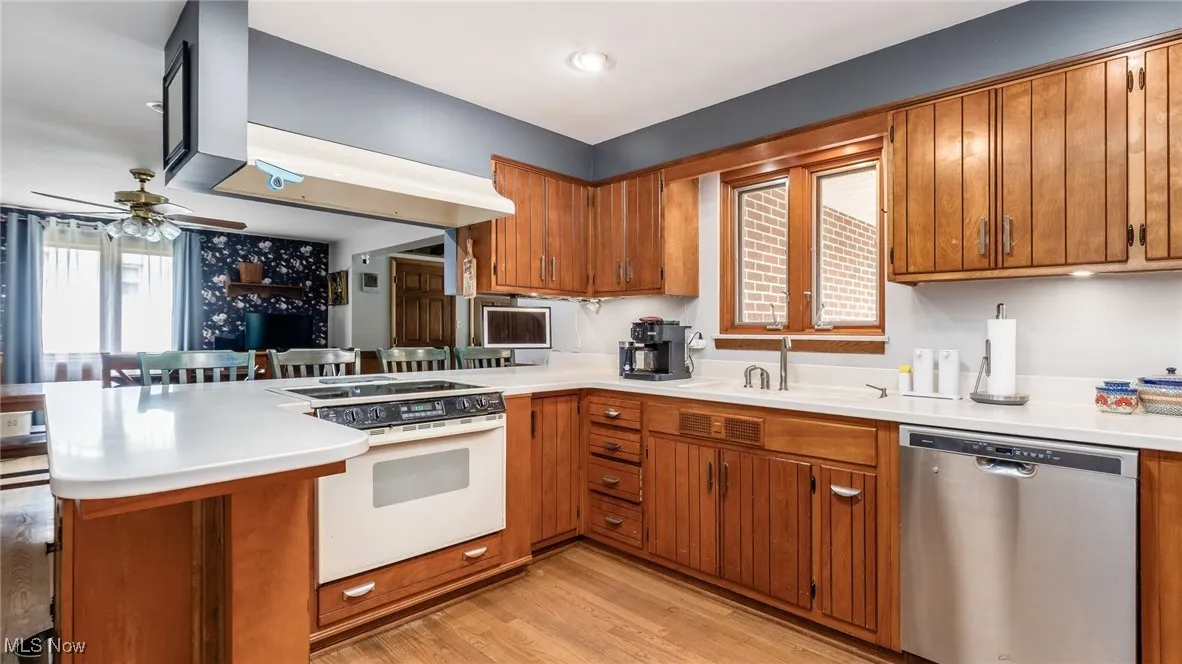 Kitchen featuring dishwasher, a peninsula, brown cabinetry, light countertops, and light wood finished floors