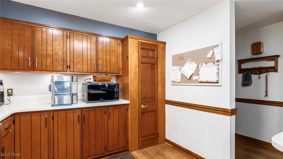 Kitchen with light wood finished floors, light countertops, black microwave, and brown cabinets