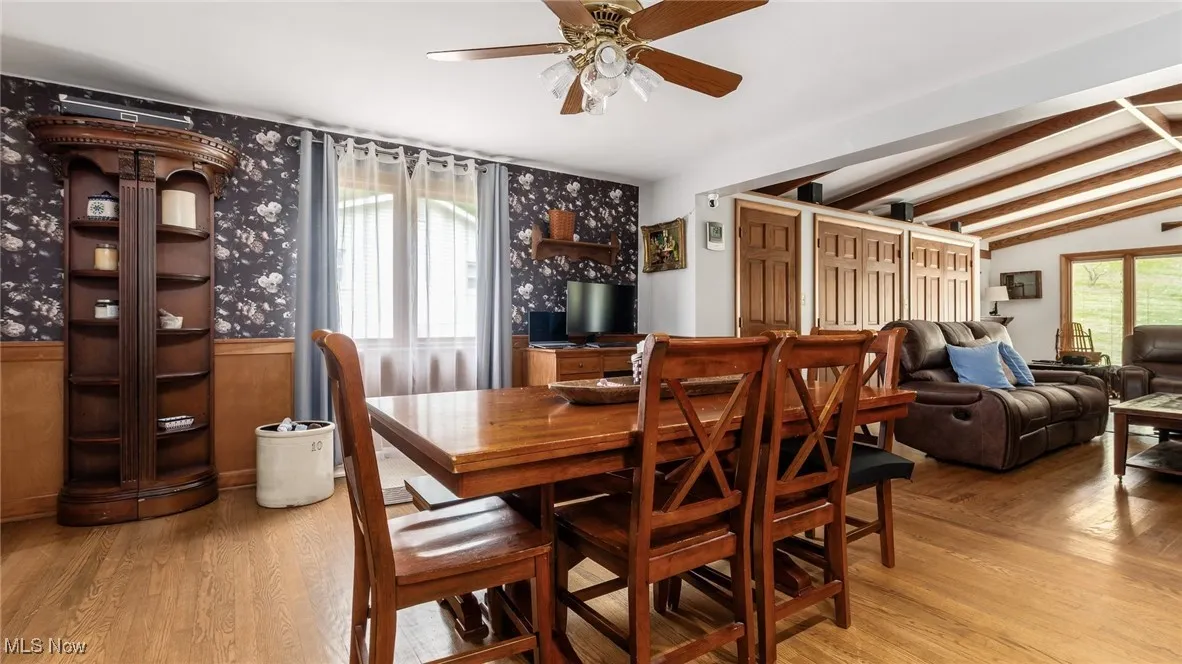 Dining room with plenty of natural light, light wood-type flooring, wallpapered walls, a wainscoted wall, and a ceiling fan