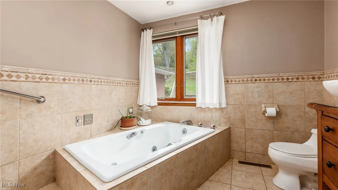 Full bathroom featuring wainscoting, tile walls, a whirlpool tub, and light tile patterned floors