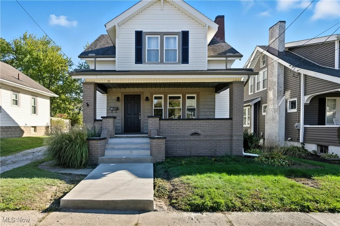 View of front of home with a porch, a front yard, a shingled roof, and brick siding
