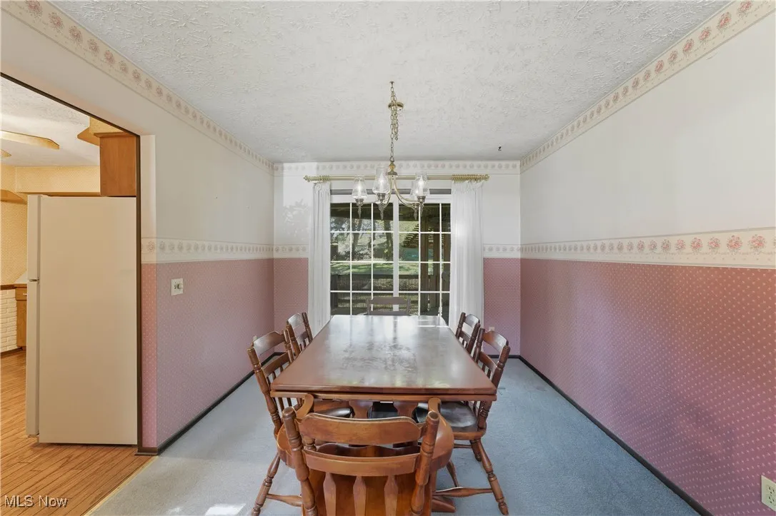 Dining space with a textured ceiling, a wainscoted wall, wallpapered walls, and a chandelier