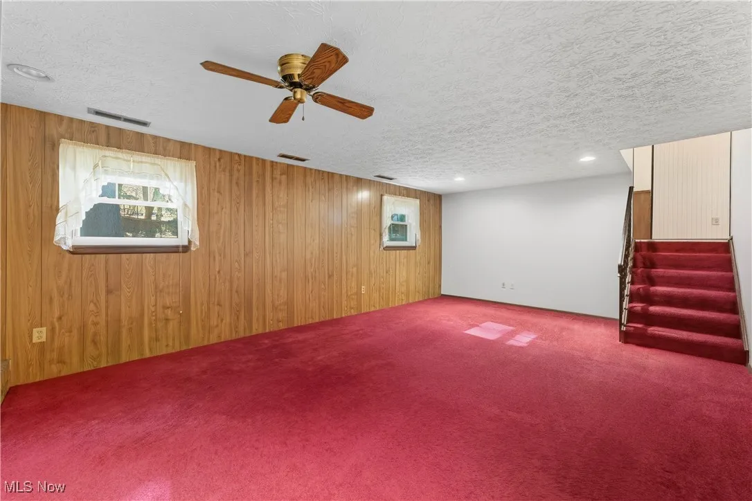 Below grade area featuring carpet flooring, wooden walls, a textured ceiling, stairway, and a ceiling fan