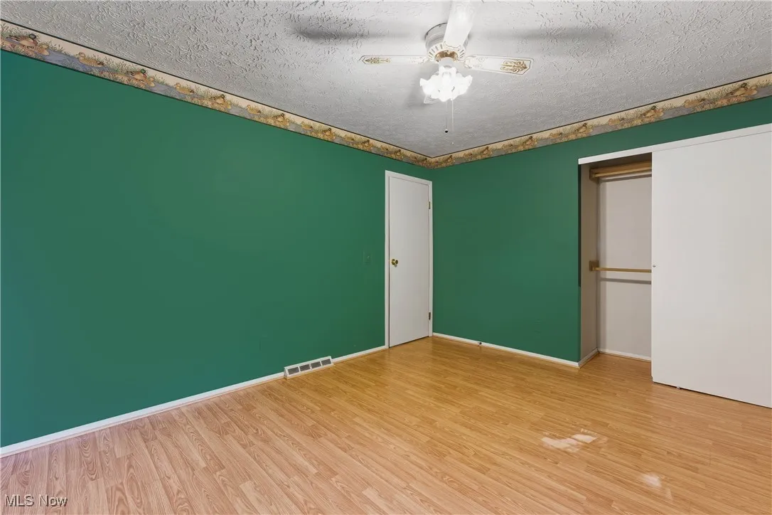 Unfurnished bedroom with light wood-style flooring, a textured ceiling, a ceiling fan, and a closet