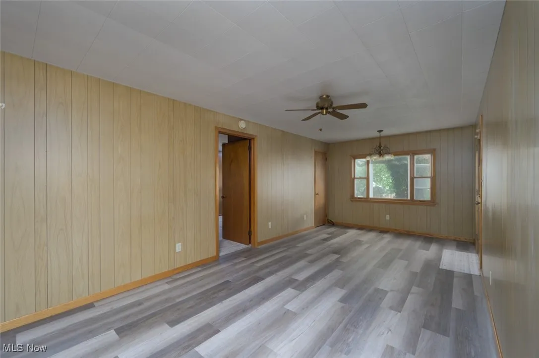 Unfurnished room with light wood-style floors, a ceiling fan, and wooden walls