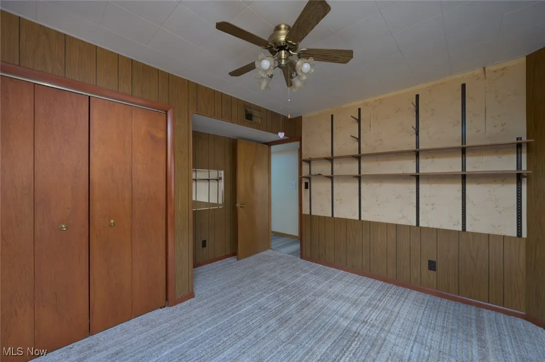 Unfurnished bedroom with wood walls, carpet floors, ceiling fan, and a closet