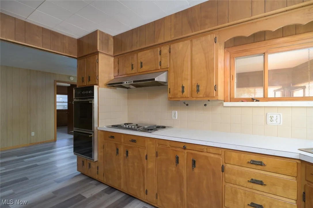 Kitchen with light countertops, brown cabinets, dark wood-style floors, tasteful backsplash, and wooden walls